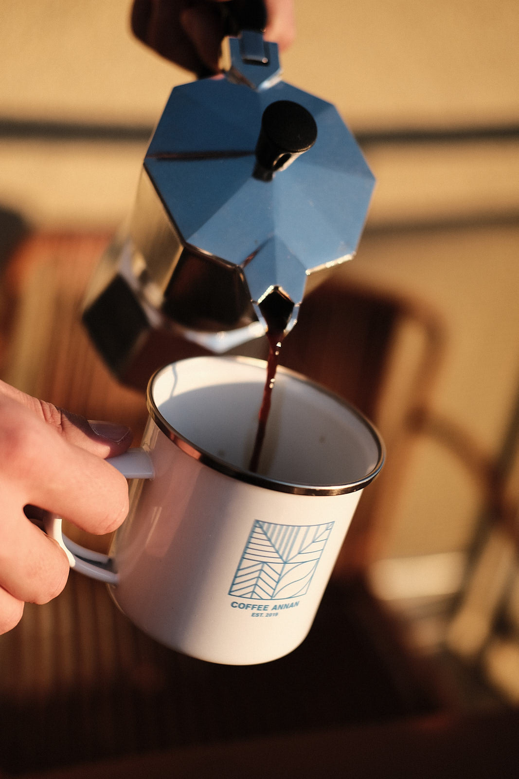 Kaffee wird aus Bialetti-Mokkakanne in Tasse mit Coffee Annan Logo gegossen