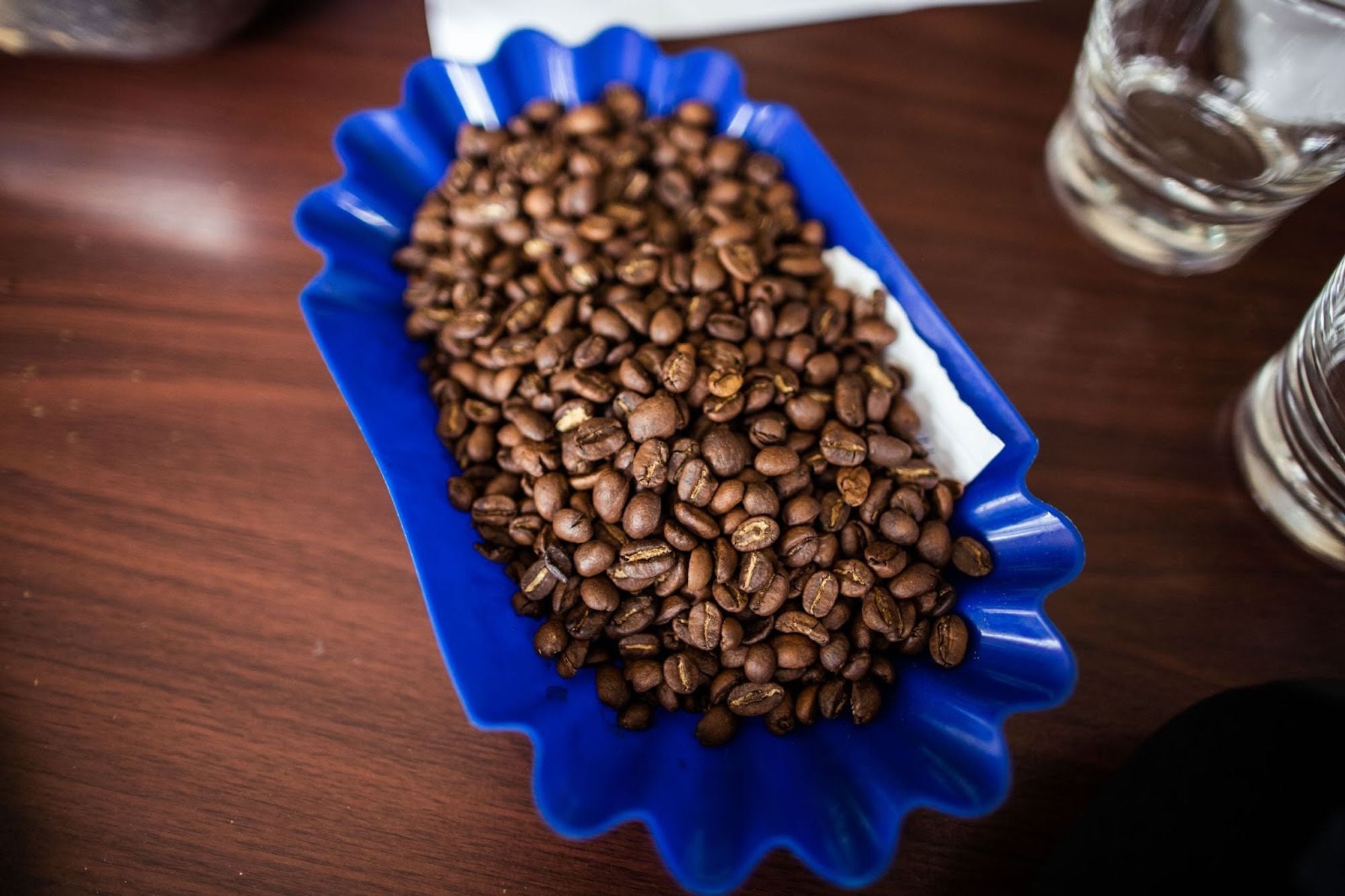 Geröstete Kaffeebohnen in einer blauen Probierschale auf Holztisch